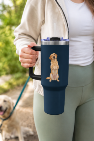 Woman holding a navy 40 oz thermal tumbler with a black handle and begging Yellow Labrador design while walking a Yellow Lab outdoors.